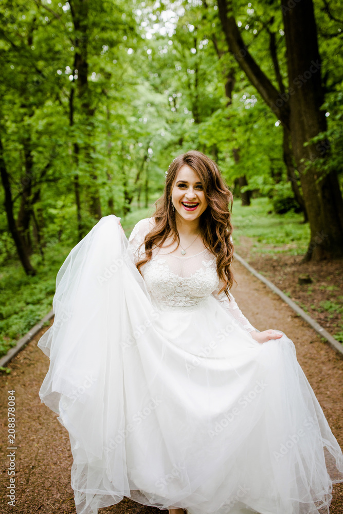 An magnificent woman in a white dress walks along the path in the park