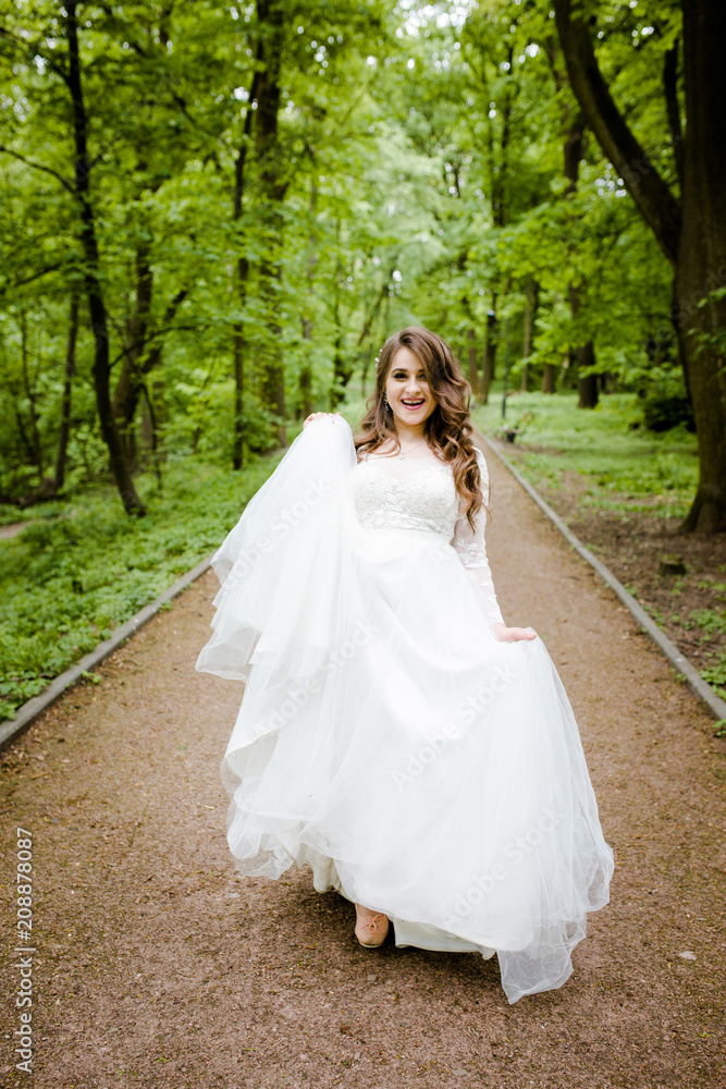 An magnificent girl in a white dress walks along the path in the park