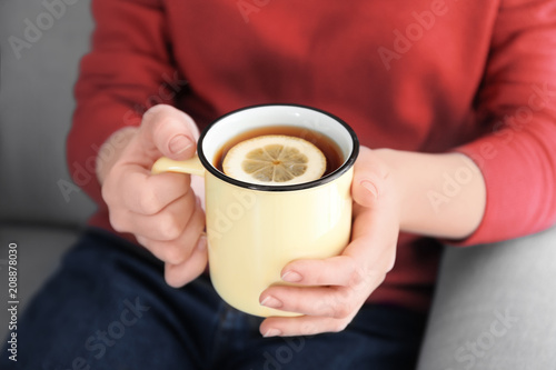 Young woman holding mug of hot aromatic tea with lemon, closeup