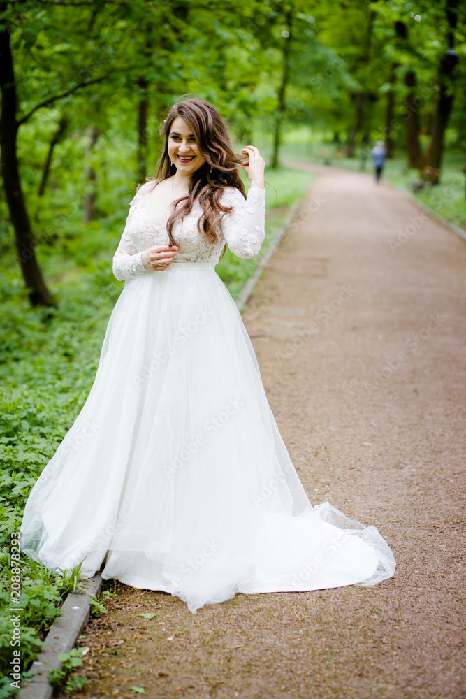 An stunning girl in a white dress walks along the path in the park