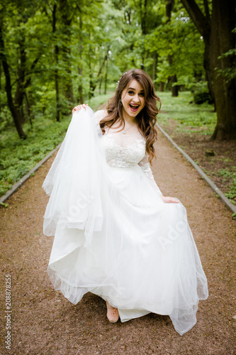 An emotional girl in a white dress walks along the path in the park