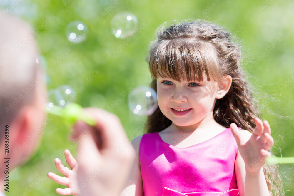 Little girl is playing with soap bubbles. Parents let the soap bubbles on their daughter in the summer in the park. Little girl is playing with soap bubbles. Parents let the soap bubbles on their daughter in the summer in the park.