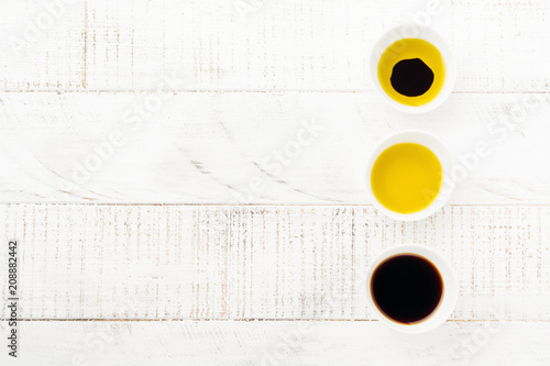 Soy sauce, olive oil and balsamic sauce in ceramic bowls on white wooden background. Top view.