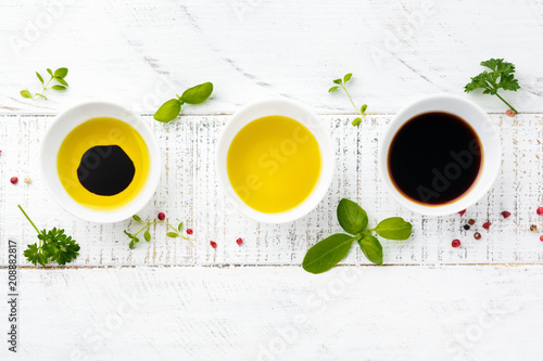 Soy sauce, olive oil and balsamic sauce with herbs basil, parsley, pepper and thyme on white wooden background. Top view.