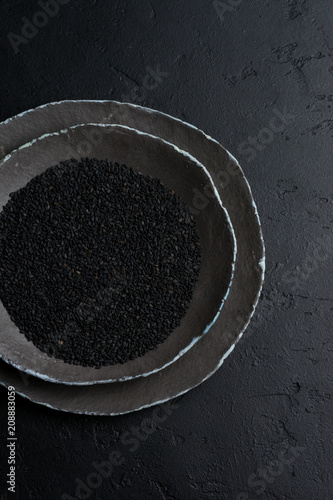 Black sesame seeds in black ceramic plates on a dark old vintage background. Rustic style. Top view.