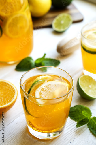 Iced lemonade pitcher & two glasses, wooden juicer, cold citrus infused water, lemon & lime, mint leaves, cutting board on white wooden windowsill. Apartment window background, close up, copy space.