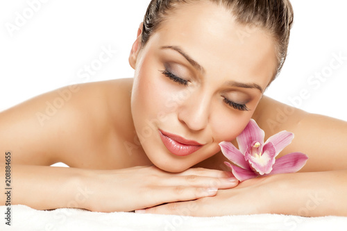a pretty young woman lying with orchid on a white background