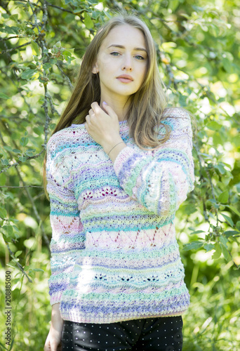 The blonde with blue eyes  in a knitted pullover  poses outdoors