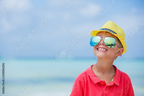 Happy child in yellow hat and sunglasses on beach. Summer vacation concept