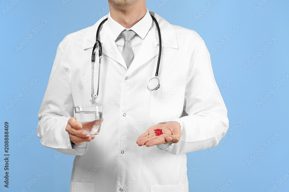 Male doctor holding glass of water with pills on color background Male doctor holding glass of water with pills on color background