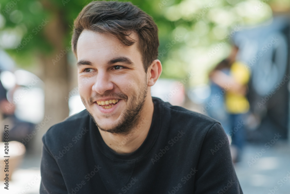 Close up portrait of a happy young American man laughing outdoor. Young man relaxing on park bench on a summers day Close up portrait of a happy young American man laughing outdoor. Young man relaxing on park bench on a summers day