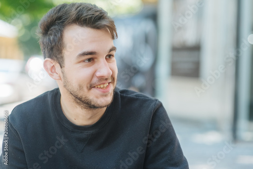 Close up portrait of a happy young American man laughing outdoor. Young man relaxing on park bench on a summers day
