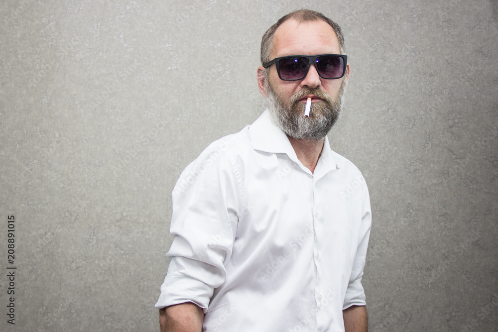 A man in a shirt with a beard in glasses smokes a cigarette