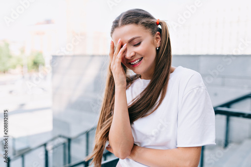 Live portrait of smiling young woman holding hand on the face and smiles with closed eyes. True emotions, positive, adorable smile, summer walks outdoor