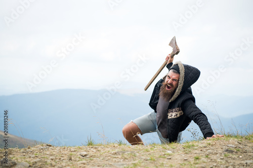Εκτύπωση καμβά Man with beard on shouting face conquers top of mountain with axe, sky background