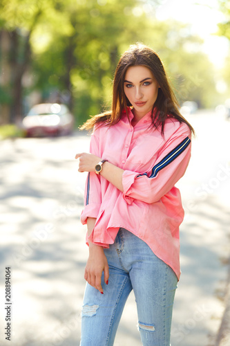 Fototapeta Naklejka Na Ścianę i Meble -  Portrait of Young and beautiful woman in casual clothes in the street. dressed in a pink shirt and jeans. spring / summer concept. relax time. girl with blue eyes. Enjoy street sunset