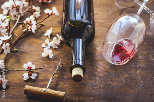 a bottle of wine. glasses with red wine. flowering branch of fruit tree. on a wooden background.