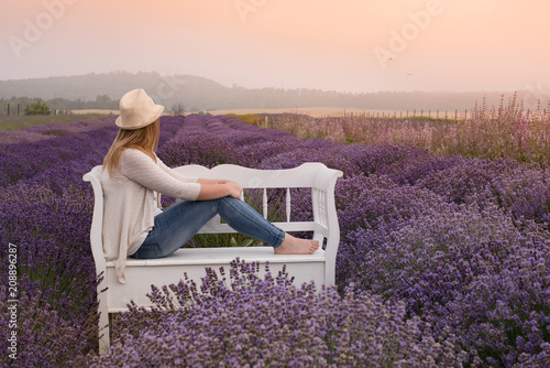 Beautiful young woman wearing a hat is sitting on a bench on the lavender field photo