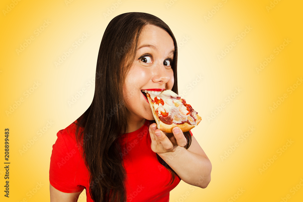 Young beautiful woman eats pizza and smiles, on yellow background.