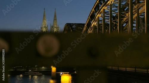 Camera rises to Hohenzollernbrucke and Cologne Cathedral at night with lights on. Taken during blue hour as train crosses  photo