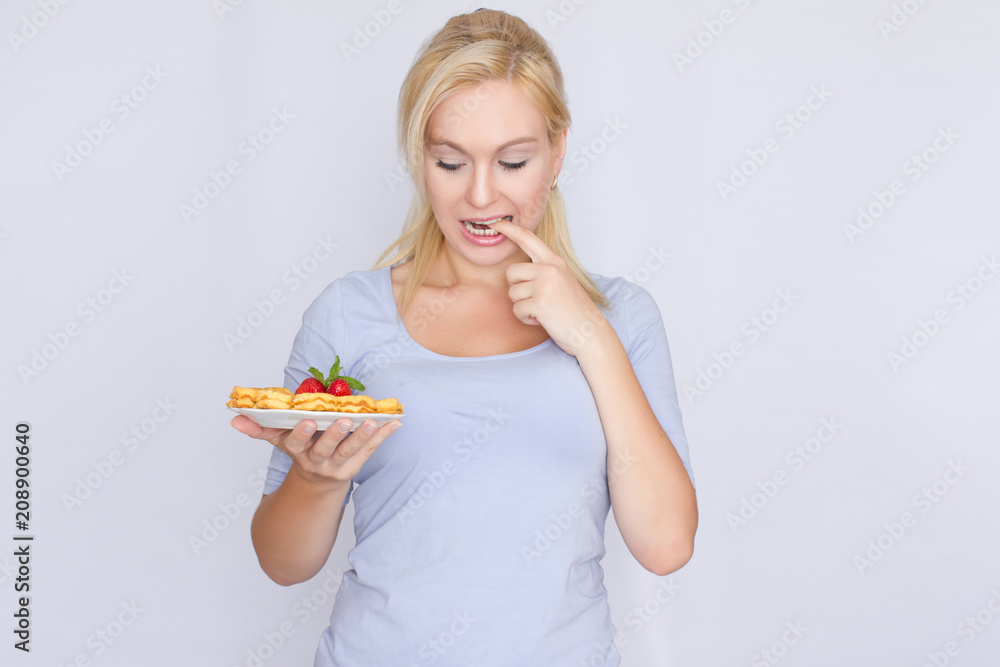 A happy blonde is holding a plate with Belgian waffles in her hands. Breakfast is decorated with strawberries and mint leaves. Concept: home food.