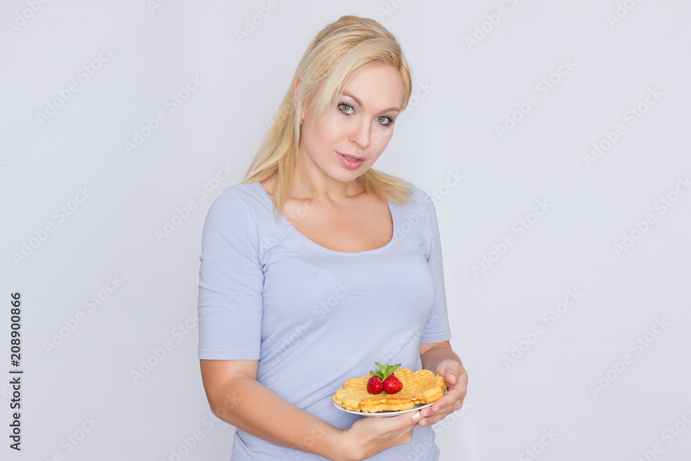 A happy blonde is holding a plate with Belgian waffles in her hands. Breakfast is decorated with strawberries and mint leaves. Concept: home food. A happy blonde is holding a plate with Belgian waffles in her hands. Breakfast is decorated with strawberries and mint leaves. Concept: home food.