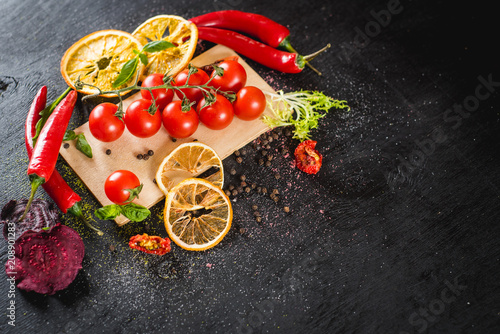 Fresh cherry tomatoes and spices on black background. Top view. Copy space