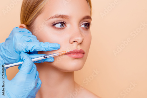 Perfection wellness wellbeing concept. Close up cropped portrait of stylish pretty nude natural model getting cosmetic botox injection in lips, shape correction, isolated on beige background