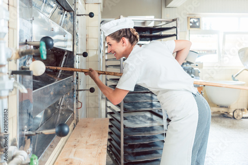 Baker woman getting bread out of bakery oven in her bakery
