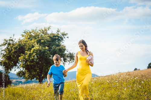 Mother with her son running on a summer meadow in the grass
