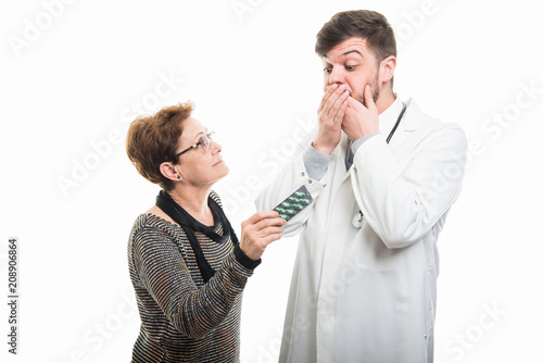 Male doctor covering mouth and female patient showing pills