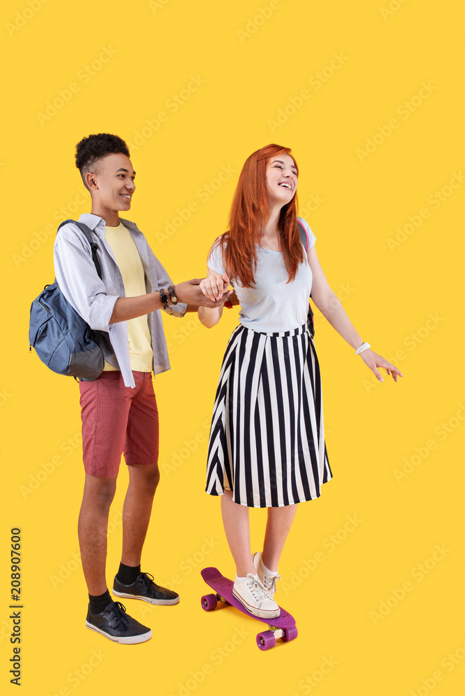 New experience. Nice joyful woman holding her boyfriends hand while learning to skateboard New experience. Nice joyful woman holding her boyfriends hand while learning to skateboard