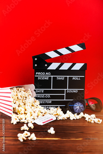 Film watching. Popcorn, clapperboard and glasses on wooden and red background