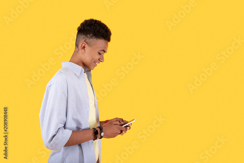Social networking. Cheerful young man looking at his smartphone while typing a message
