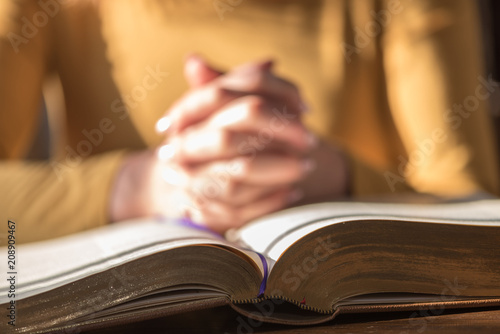 Woman praying with her hands over the bible, hard light