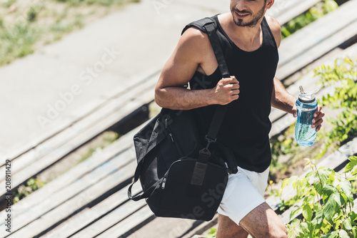 Fototapeta Naklejka Na Ścianę i Meble -  cropped image of sportsman holding bottle of water and bag for sport equipment on stairs at sport playground