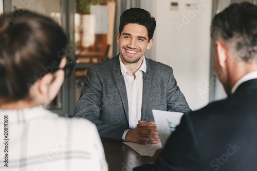 Business, career and placement concept - young caucasian man smiling, while sitting in front of directors during corporate meeting or job interview