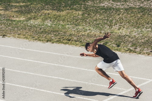 young male sprinter taking off from starting position on running track
