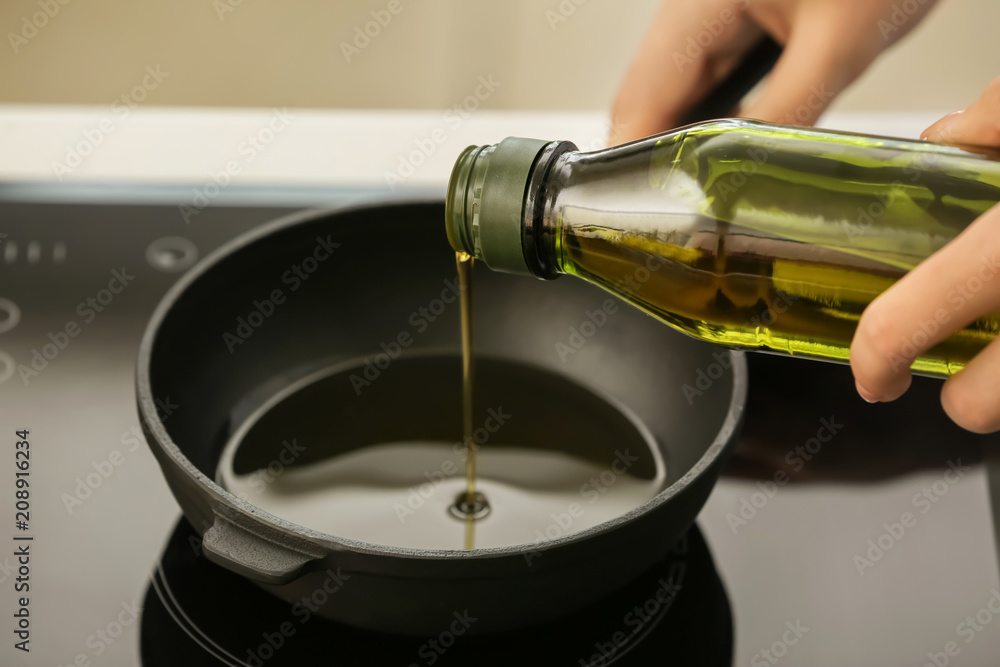 Woman pouring olive oil into frying pan on stove Woman pouring olive oil into frying pan on stove