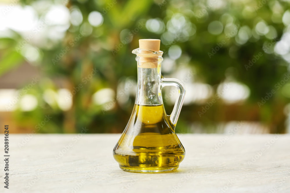 Jug with olive oil on table against blurred background