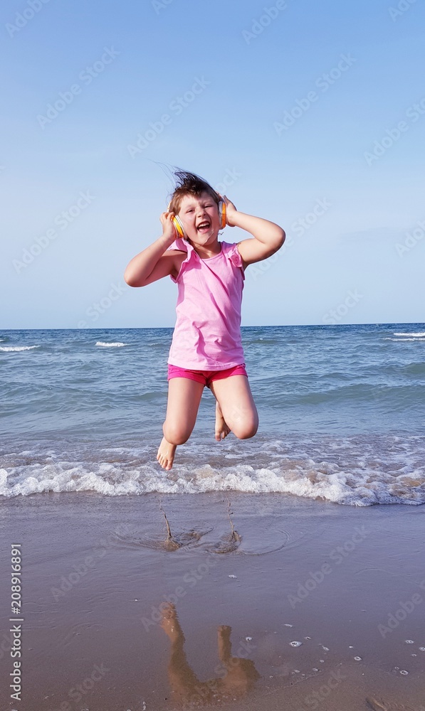 Bambina che salta in spiaggia ascoltando musica con le cuffie Bambina che salta in spiaggia ascoltando musica con le cuffie