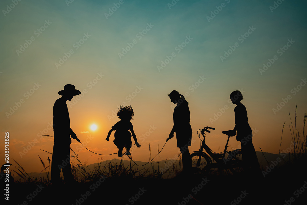 Group of happy children playing on meadow at sunset, silhouette