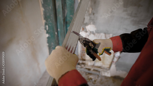 Construction worker uses metall cutting scissors to cut metall drywall profiles. photo