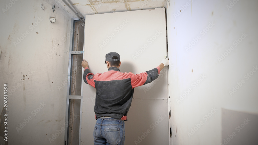 man is lifting up and adjusting a plasterboard on an aluminum construction, building works inside a new apartment man is lifting up and adjusting a plasterboard on an aluminum construction, building works inside a new apartment