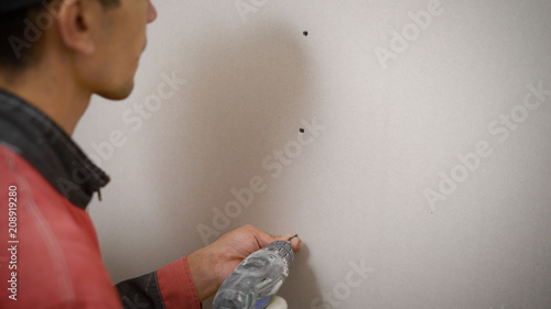 A professional builder makes symmetrical holes in a plasterboard wall using an electric drill, a man screws the wall with bolts or nails