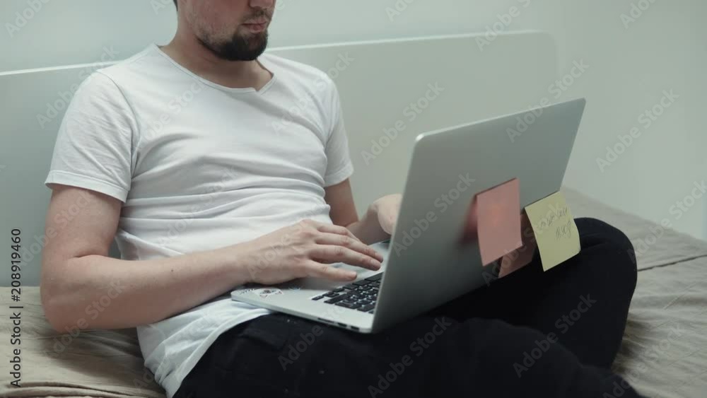 Adult man is spending the day in bed with laptop writing a blog online. Man has a laptop in his knees while lying. Nice interior. Adult man is spending the day in bed with laptop writing a blog online. Man has a laptop in his knees while lying. Nice interior.