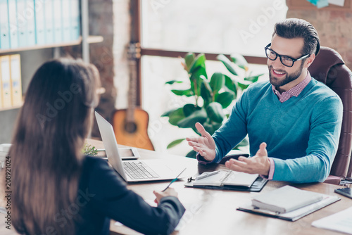 Job interview - Joyful, successful businessman asking candidate questions, sitting at desk in workplace on chair, girl making notes