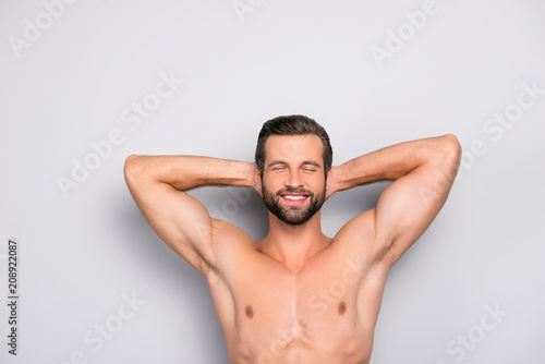 Attractive, stunning, manly, smiling macho isolated on gray background, having two arms behind the head and closed eyes, showing his shaven armpits - wellness, wellbeing concept photo