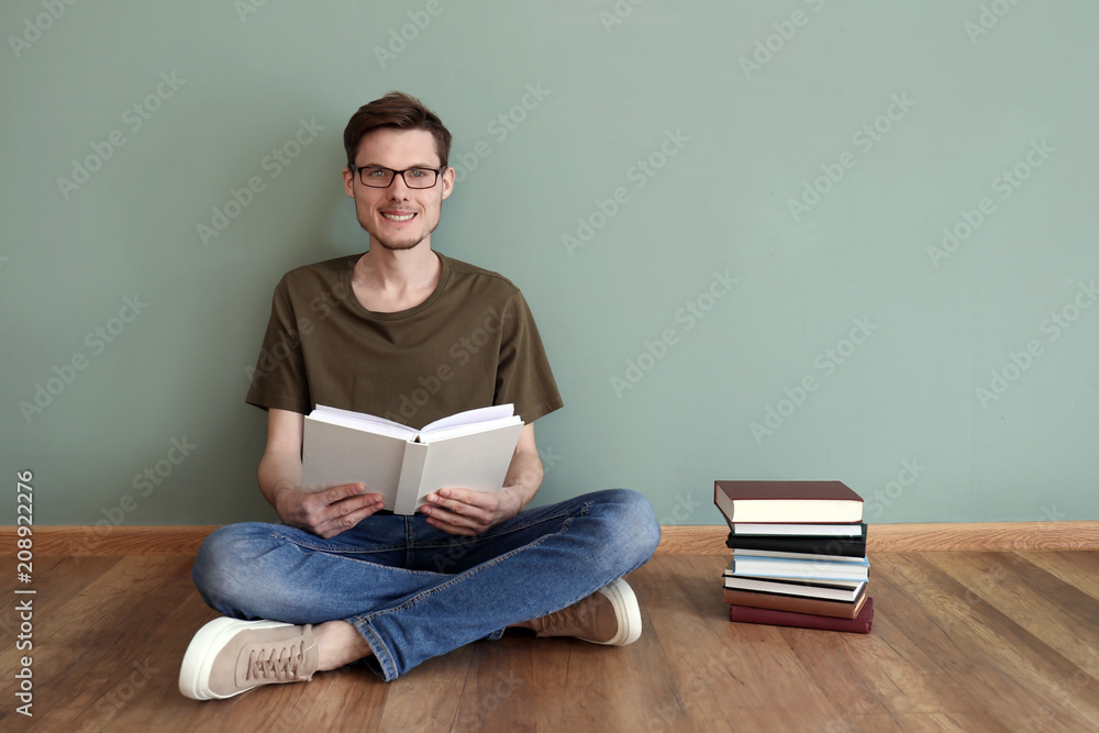 Young man reading books while sitting on floor near color wall