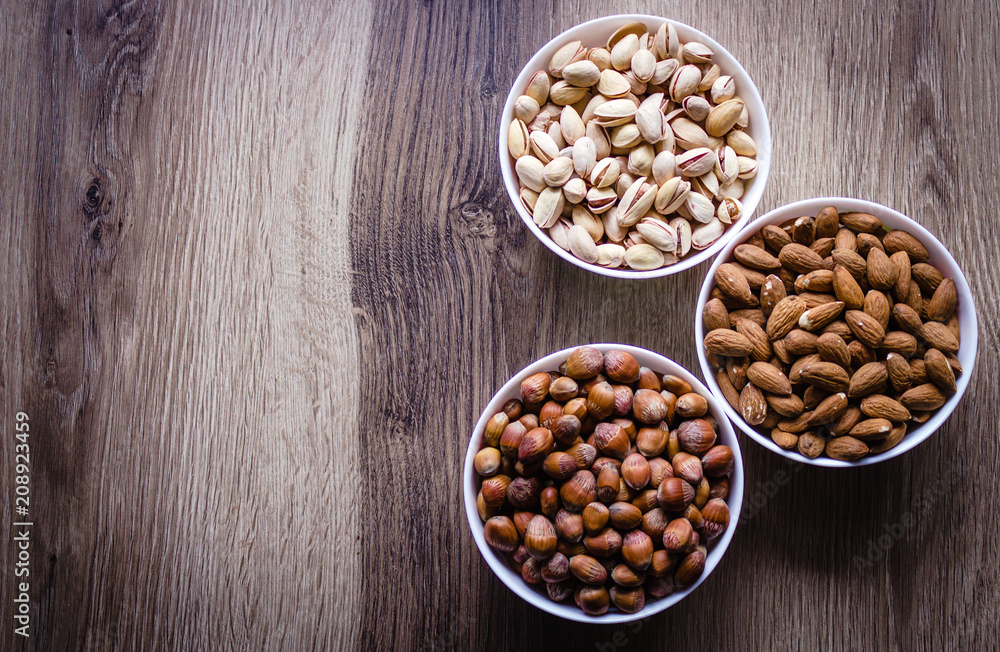 Mixed nuts in a white ceramic bowl on a wooden background.